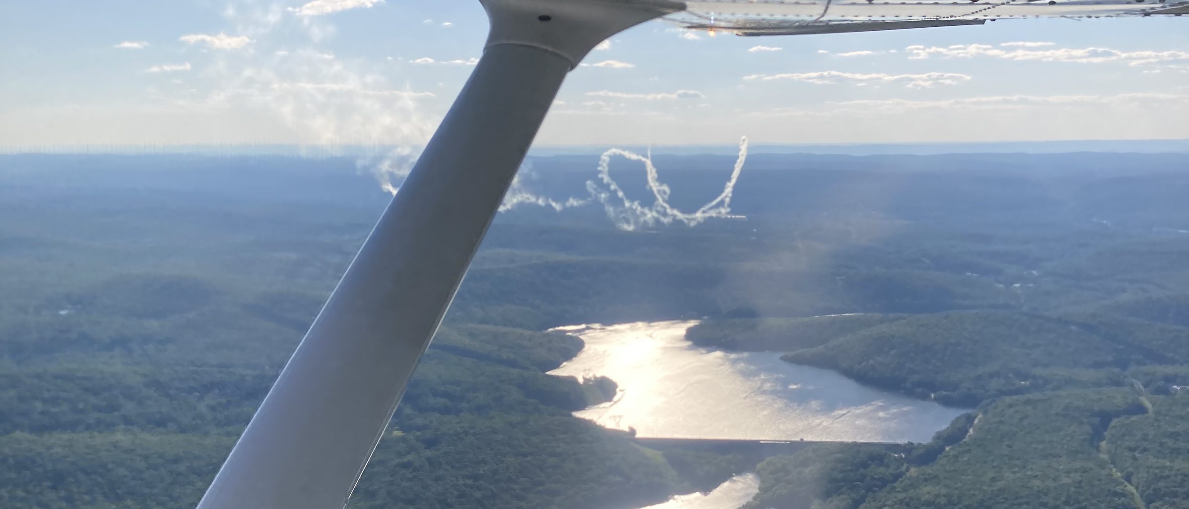 Sunlight reflecting off a river valley seen beneath the wing strut of a training aircraft.
