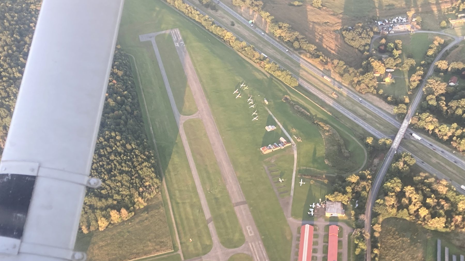 Small general aviation airport seen from the traffic pattern in golden evening light, aircraft parked along the runway.