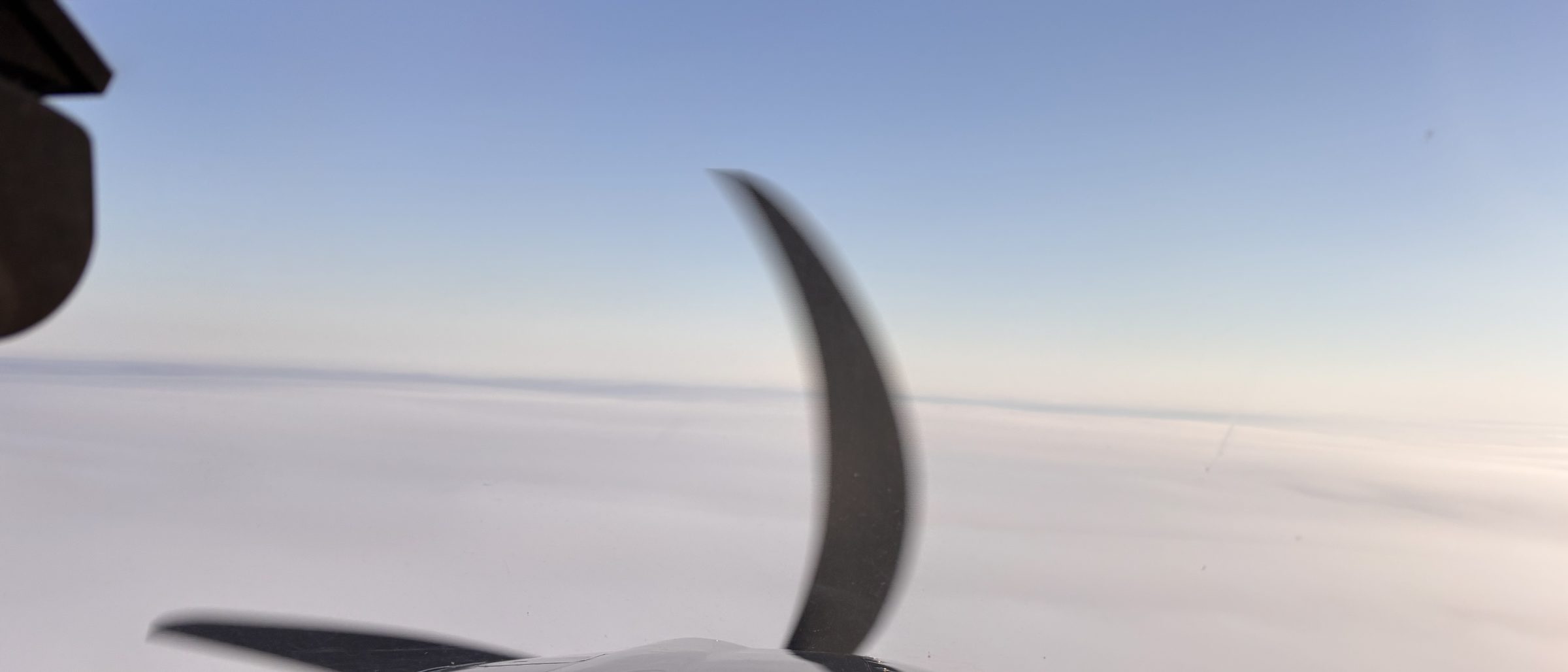 Propeller blade over an unbroken cloud deck stretching to the horizon.