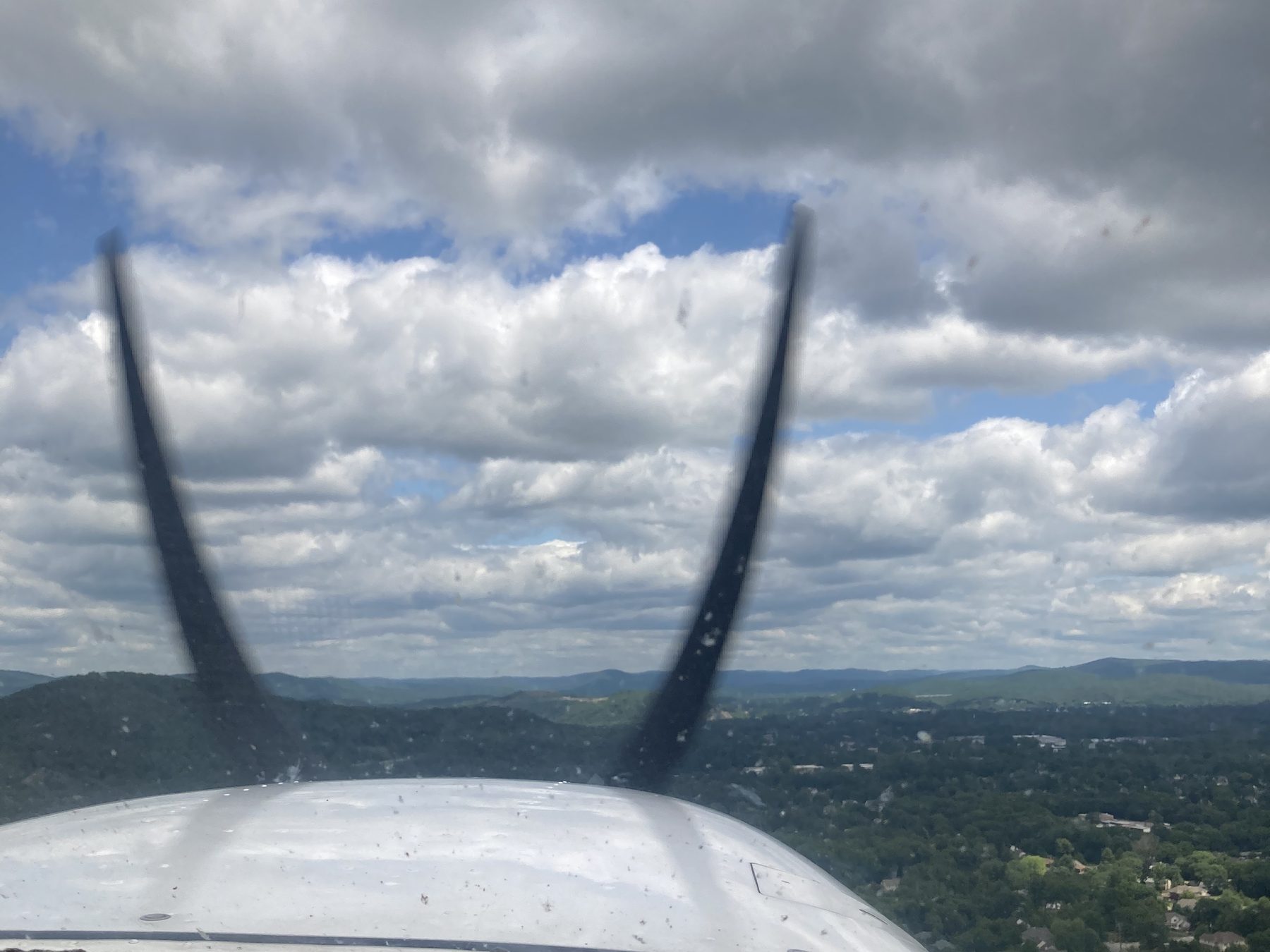 View through the windscreen of a training aircraft: propeller arcs against building cumulus clouds.