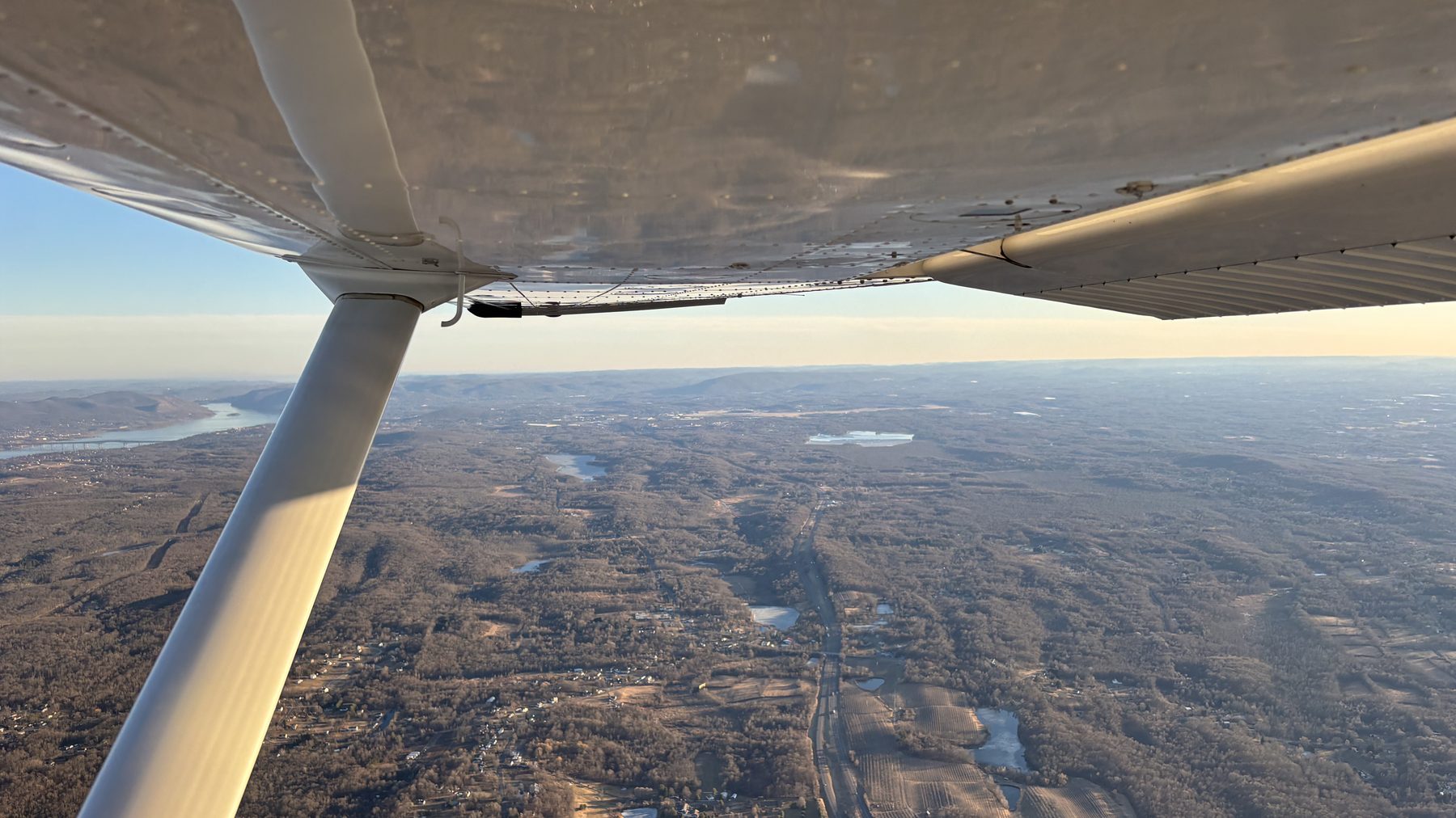 Wing and strut of a Cessna in golden light above a winter valley.