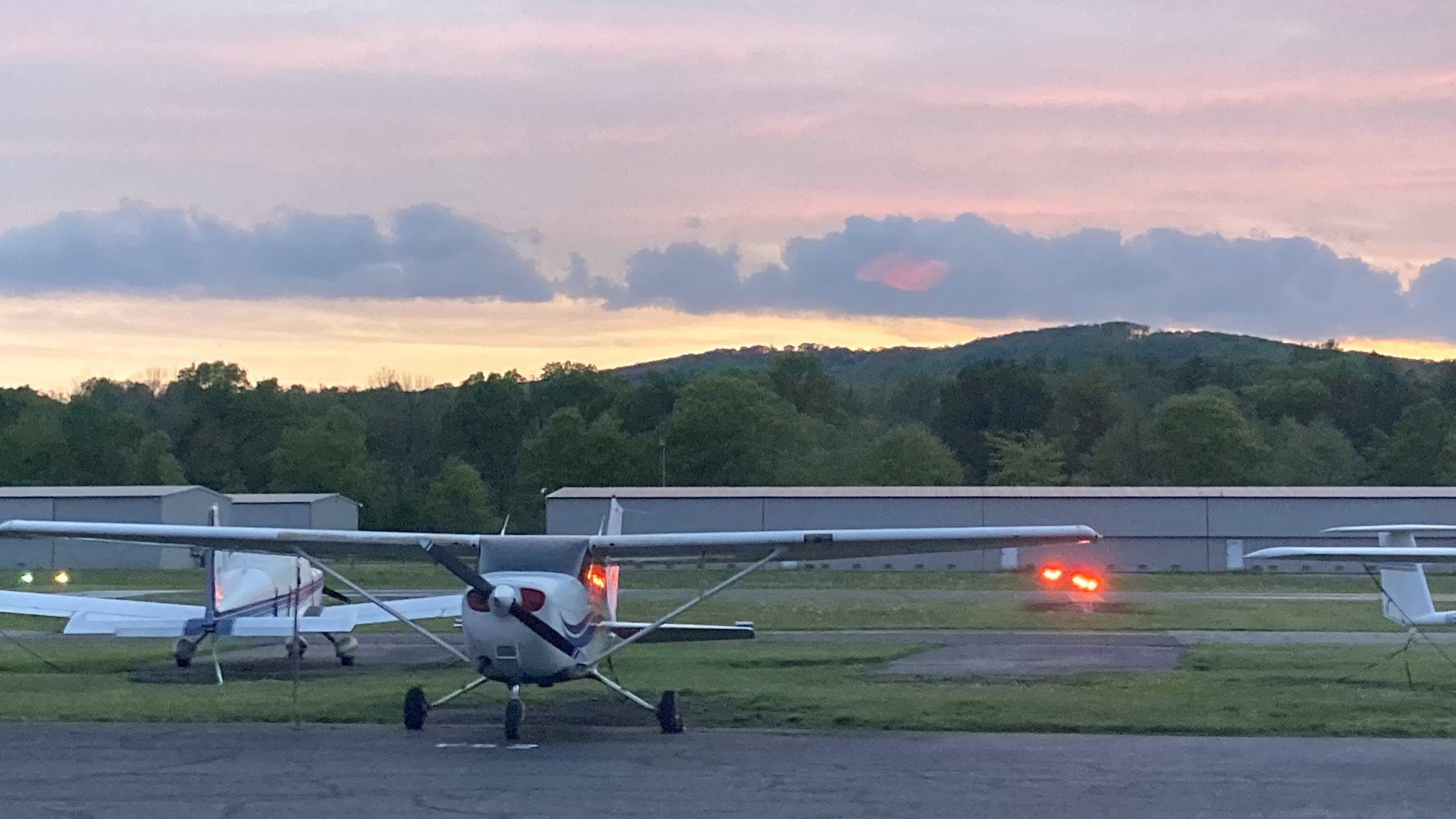 Cessna 172 parked nose-on at dusk, airport lights glowing beneath a pink evening sky.