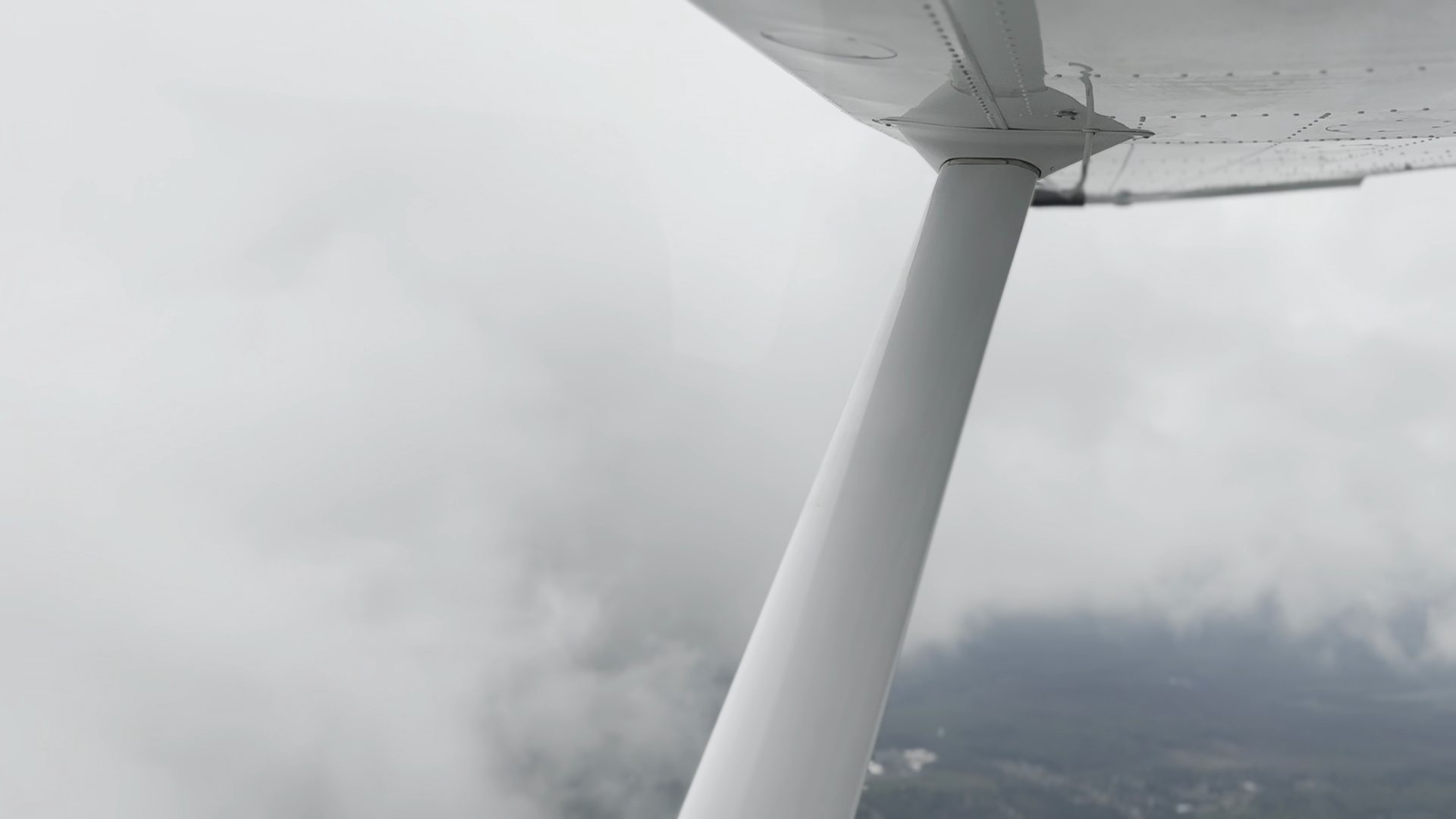 The wing strut of a training airplane disappearing into cloud, the ground barely visible below.