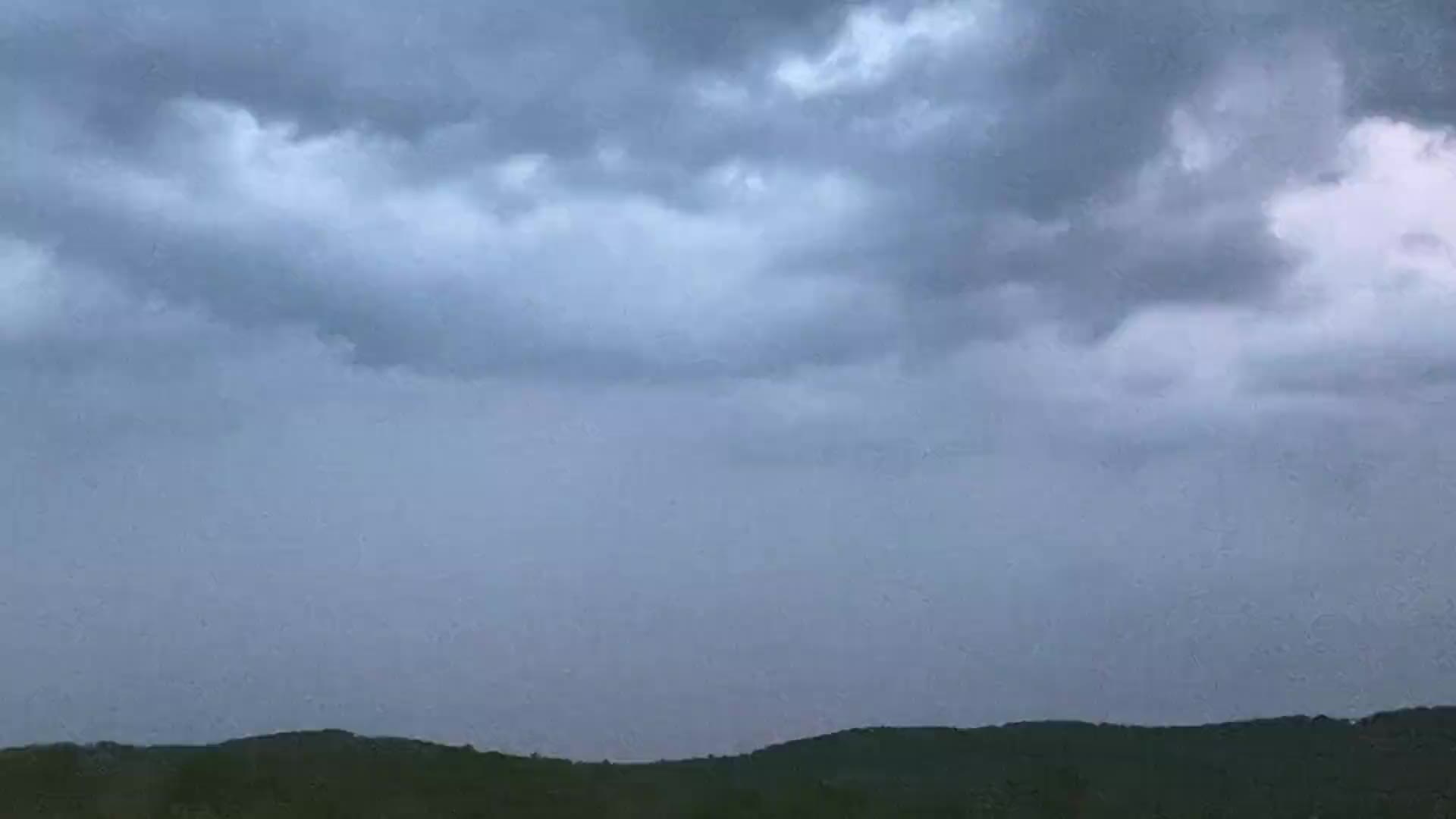 Dark storm clouds building over a wooded ridge as a thunderstorm approaches.