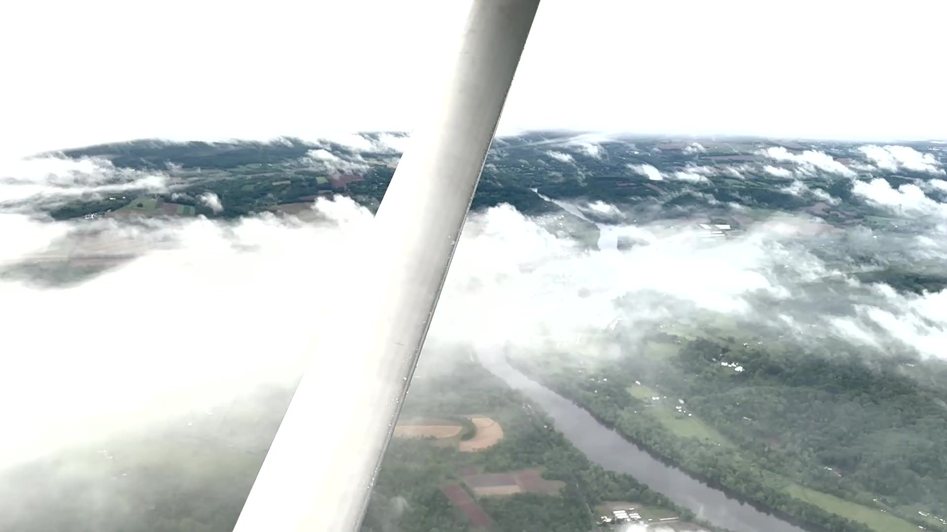 Wing and strut of a training aircraft crossing a broken cloud layer.