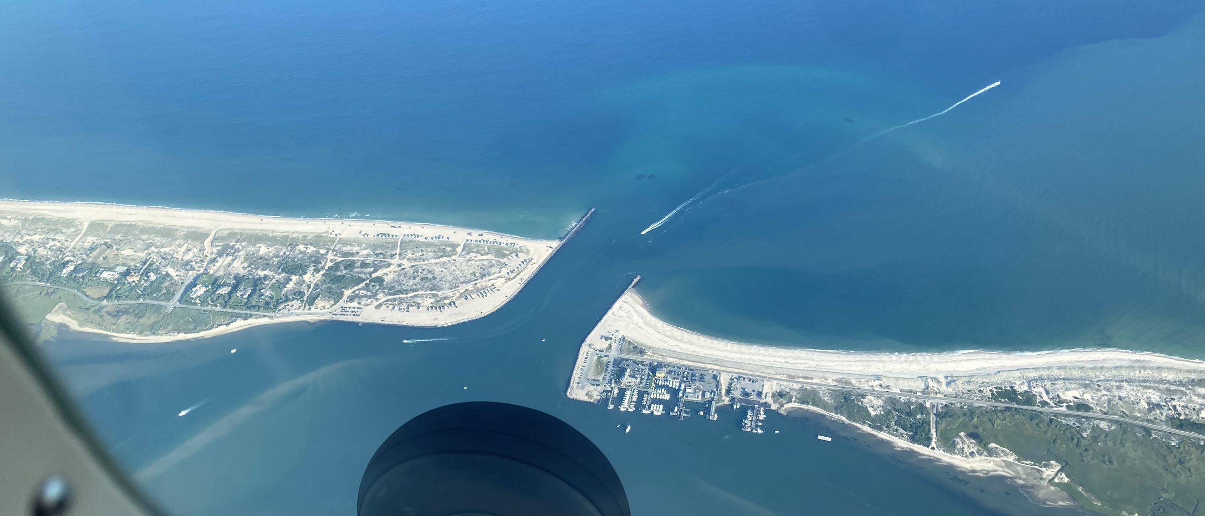 Top-down view of a coastal inlet and barrier islands from the cockpit, landing gear visible in frame.